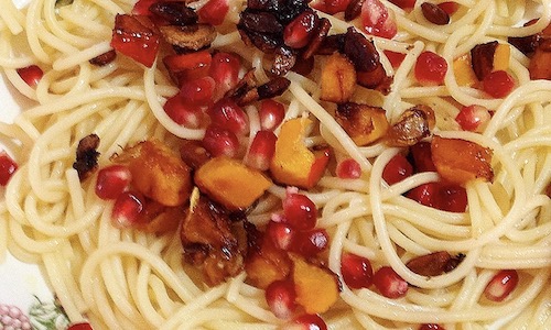 La foto muestra un plato de espagueti servido con un salteado de clabaza Hokkaido y semillas de granada.