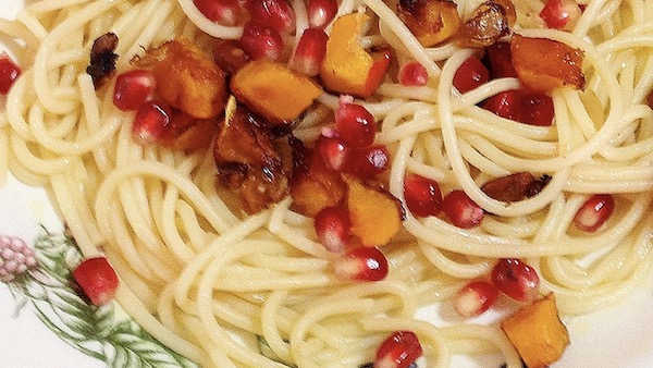 La foto muestra un plato de espagueti servido con un salteado de clabaza Hokkaido y semillas de granada.