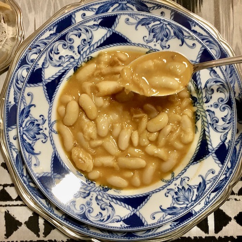 La foto muestra una fabada servida en el plato con una cucharada para comer.