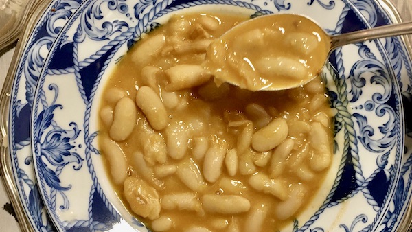 La foto muestra una fabada servida en el plato con una cucharada para comer.