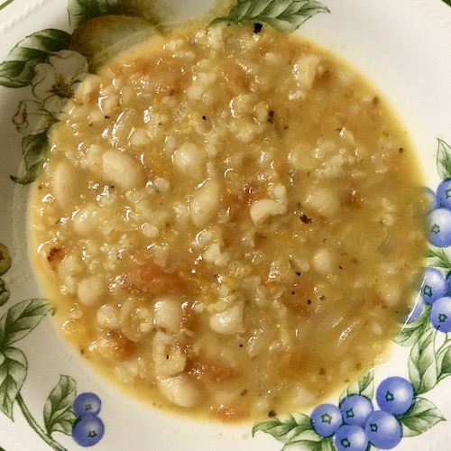 La foto muestra el caldo de alubias con arroz servido en el plato, en el que resaltan los toques rojos del tomate sobre fondo blanco.