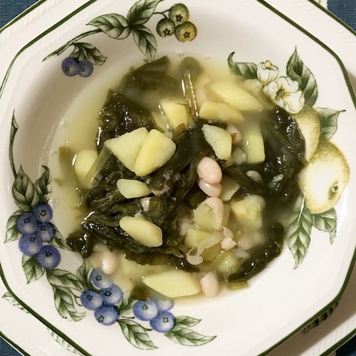 La foto muestra el caldo de grelos servido en el plato, en el que resalta el grelo, la patata y las judías blancas.