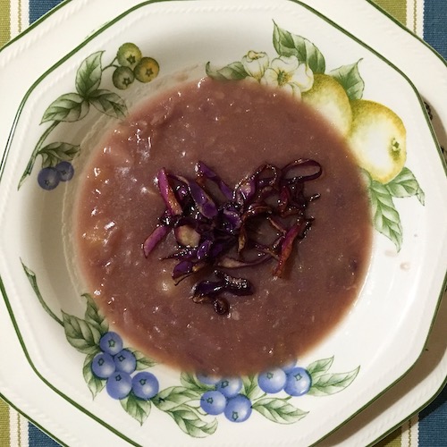 La foto muestra el caldo de lombarda servido en el plato, adornado con pequeñas tiradas de lombarda, que previamente, fueron salteadas en aceite.