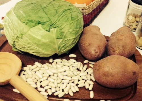 La foto muestra los ingredientes para el caldo de repollo, un repollo blanco, algunas alubias blancas y tres patatas