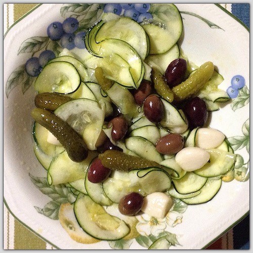 La foto muestra una ensalda de calacacín, finamente cortado en rodajas, con ajos, pepinillos y aceitunas