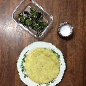 La foto muestra una tortilla servida, un recipiente con pimientos verdes y otro con sal